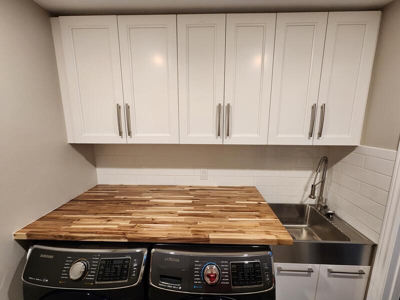Wood countertop. Stainless steel laundry sink. Painted white shaker cabinets.